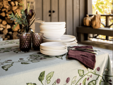 Table set with white plates and bowls on a light green tablecloth with a berry vine pattern.